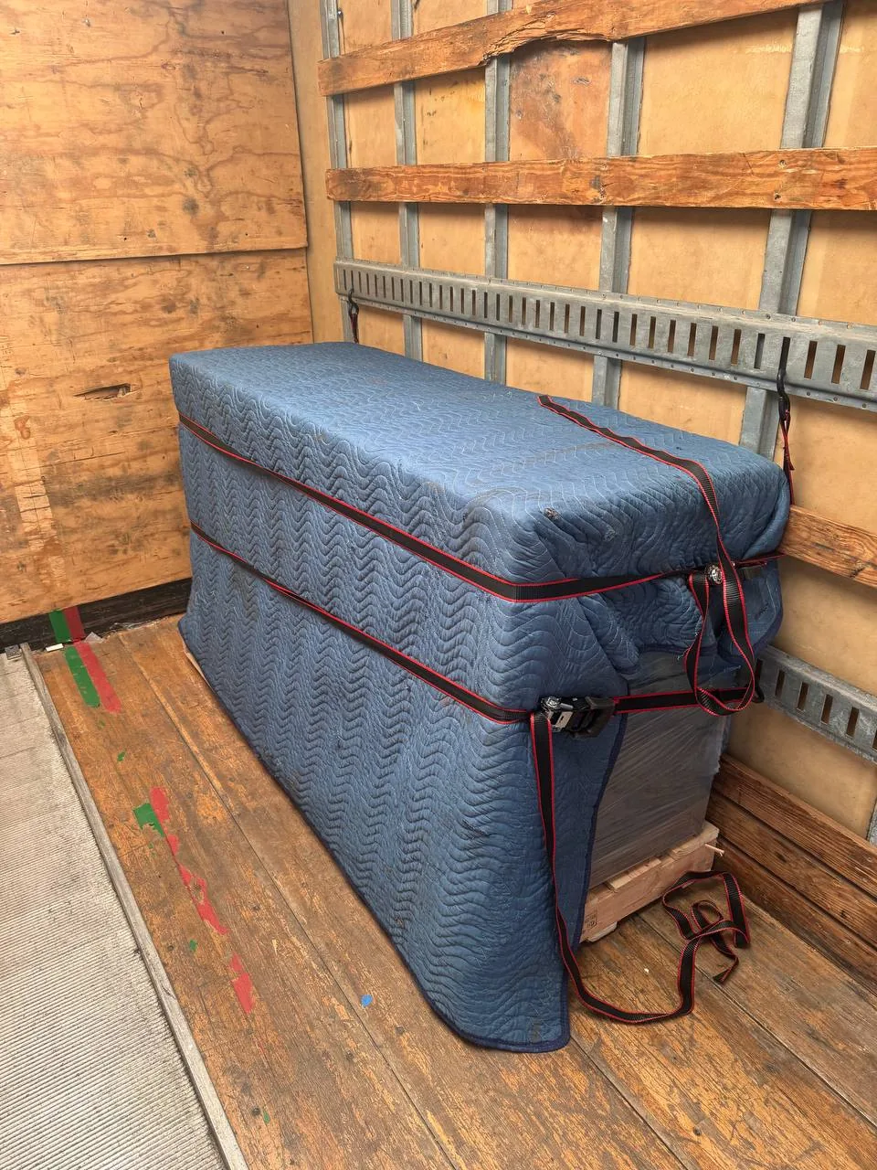 A blanket wrapped piece of furniture strapped to the wall of a truck