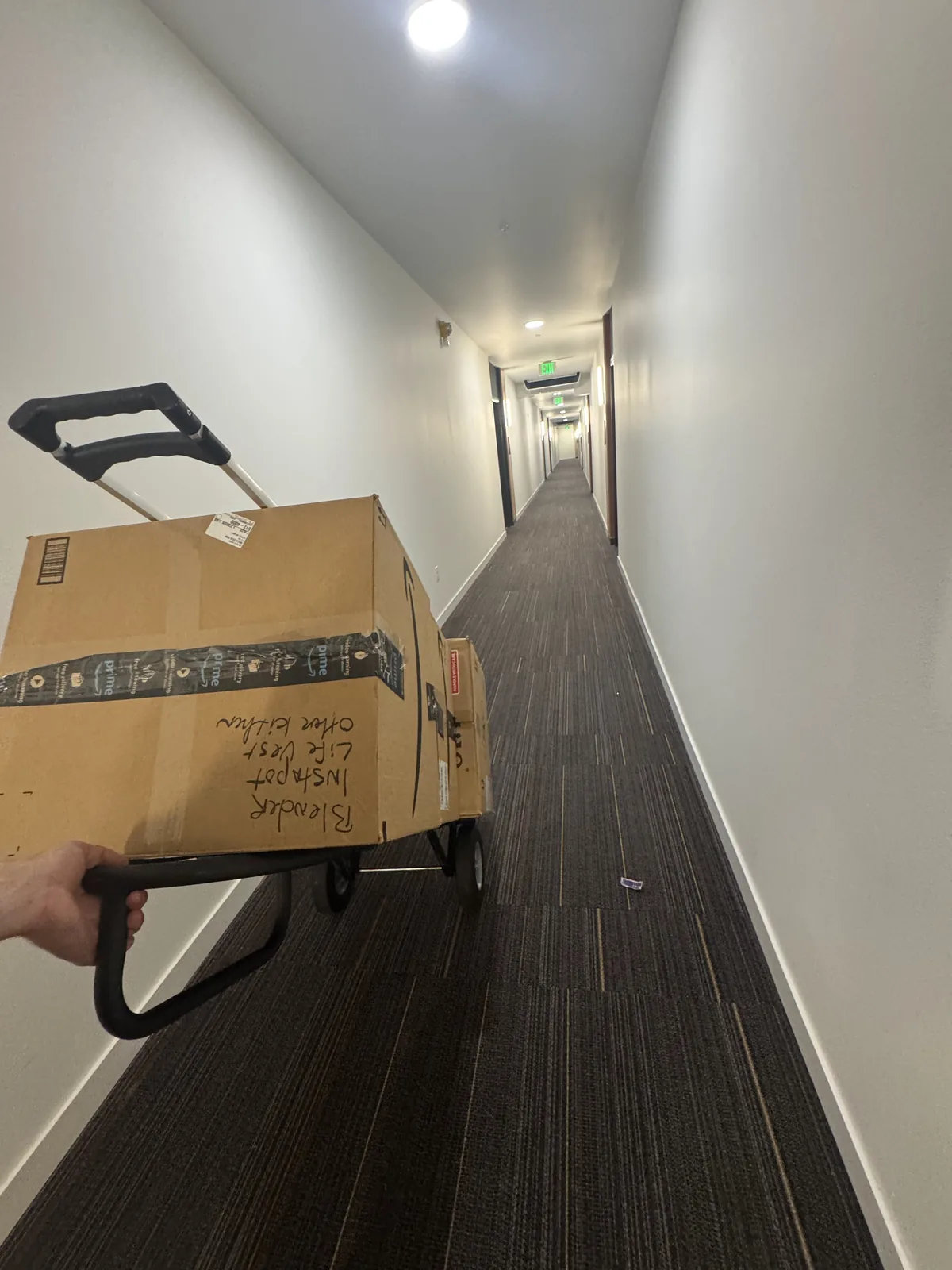 A hand truck loaded with boxes rolling down a long apartment hallway