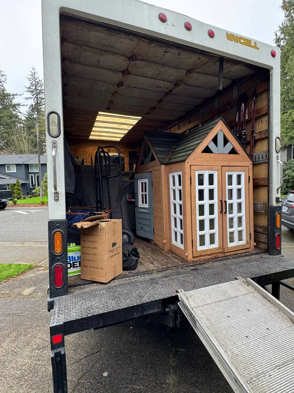 A truck with its liftgate down and a large playhouse loaded inside