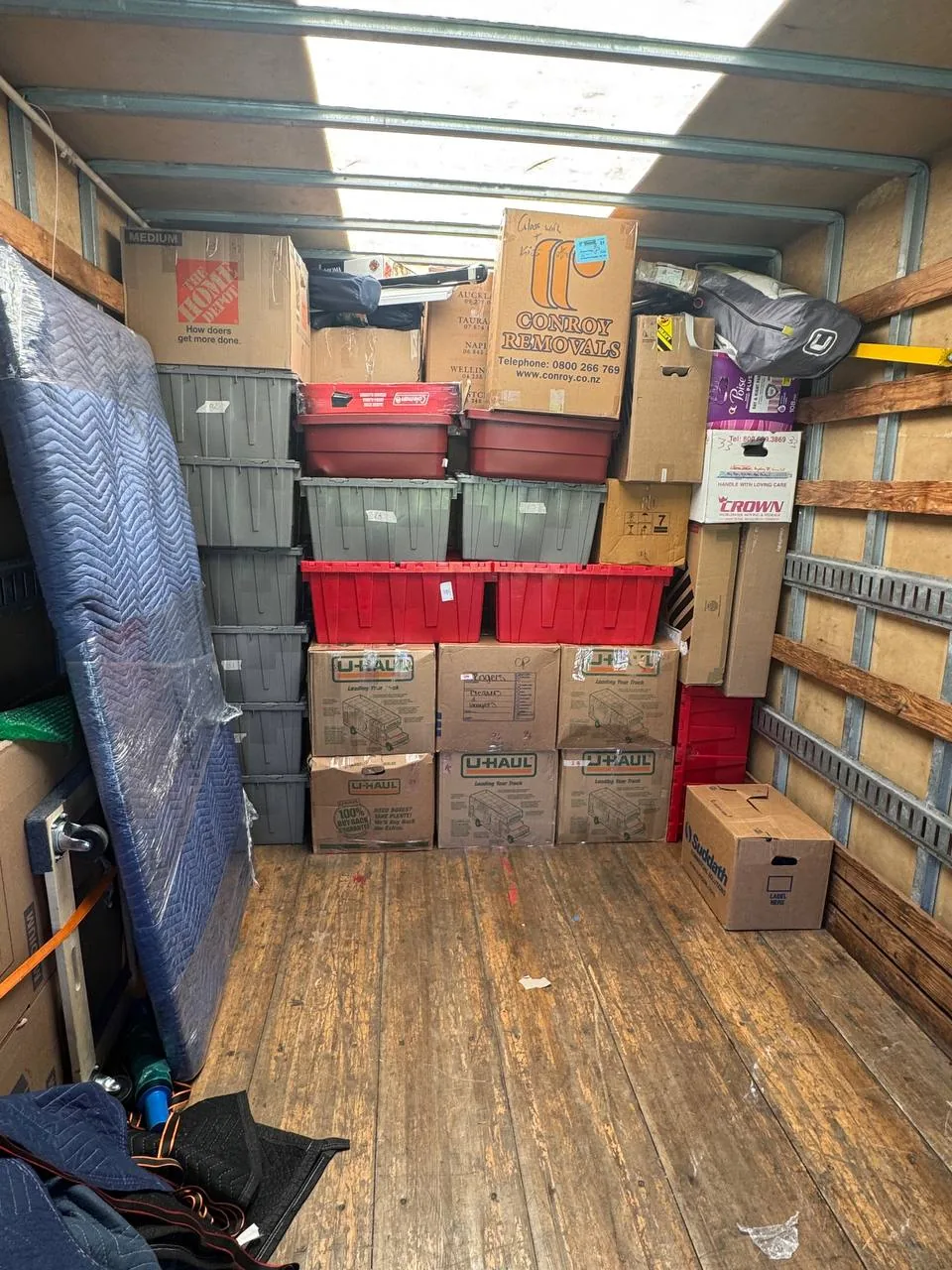 Boxes, totes and a wrapped mattress loaded and strapped inside a truck